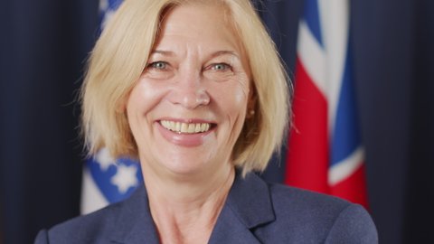 Slowmo closeup portrait of mid-adult female political leader of Caucasian ethnicity smiling at camera