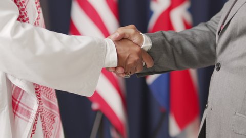 Midsection shot of two unrecognizable country leaders shaking hands in agreement. One of them wearing traditional Arab clothing and keffiyeh