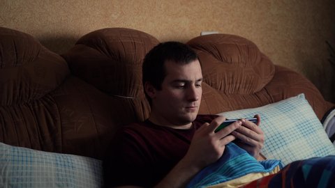 A man playing on the phone while lying on the bed