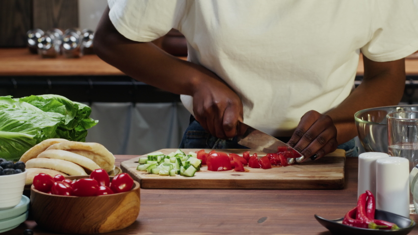 African american chef cooking vegetable salad. Woman cutting cucumbers and tomatoes on wooden board close-up. Healthy eating habits, dieting, vegetarian meal.  Royalty-Free Stock Footage #1084653625