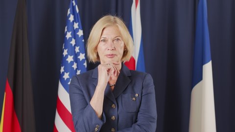 Medium slowmo portrait of mid-adult blonde Caucasian female political leader posing for camera on dark blue background