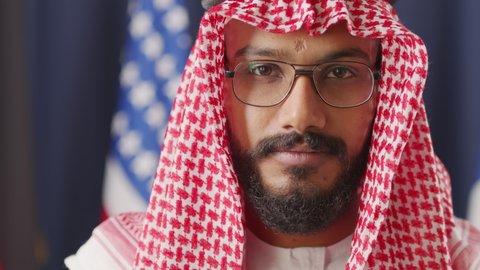Slowmo close up portrait of young male political leader of Arab country wearing keffiyeh and eyeglasses looking at camera