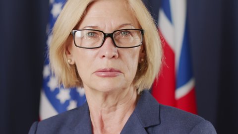 PAN closeup portrait of mid-adult female politician in formalwear and eyeglasses looking at camera