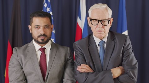 Medium portrait of two diverse male political leaders looking at camera standing on dark blue background