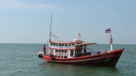 Pattaya , Chonburi , Thailand - 12 03 2021: A fishing boat docked while two fishermen walk on ropes to leave the fishing boat during a windy day at Pattaya Fishing Dock, Pattaya, Thailand.
