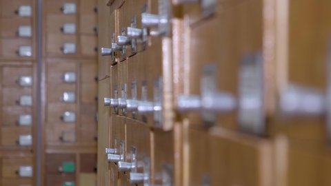 4K. Catalog cards in library. A man is looking for information in a file cabinet. Person's hands searching cards in old wooden card catalogue. Archival card index in the library