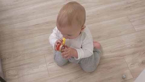 Cute happy kid playing with wooden whistle, 9-month-old baby boy sitting on the floor at home. High quality 4k footage