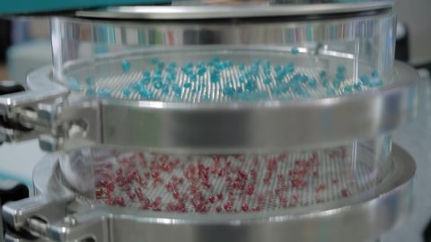 Many colorful granules bouncing on platform of sieve shaker machine for separation of particles: polymers, metal, powders, cereals, glass - close up, selective focus. Separation concept
