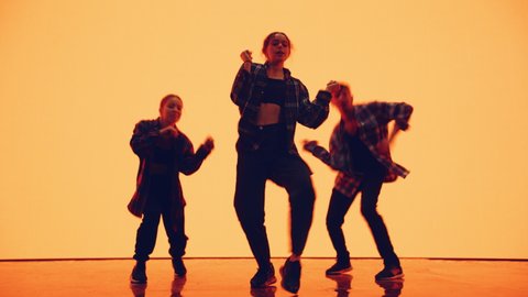 Diverse Group of Three Professional Dancers Performing a Hip Hop Dance Routine in Front of a Big Digital Led Wall Screen with Deep Warm Yellow and Orange Color Background in Studio Environment.