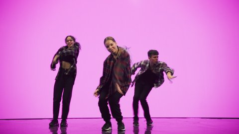Diverse Group of Three Professional Dancers Performing a Hip Hop Dance Routine in Front of a Big Digital Led Wall Screen with Deep Pink Color Background in Studio Environment.