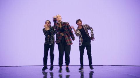 Diverse Group of Three Professional Dancers Performing a Hip Hop Dance Routine in Front of a Big Digital Led Wall Screen with Deep Purple and Violet Color Background in Studio Environment.