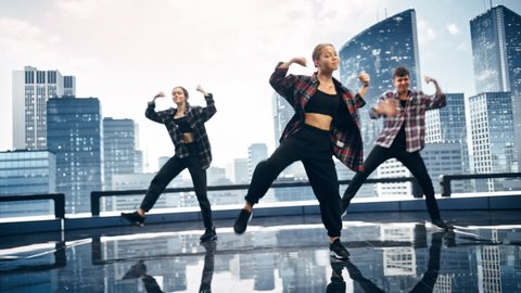 Diverse Group of Three Professional Dancers Performing a Hip Hop Dance Routine in Front of a Big Digital Led Wall Screen with Modern Urban Skyline with Office Skyscrapers in Studio Environment.
