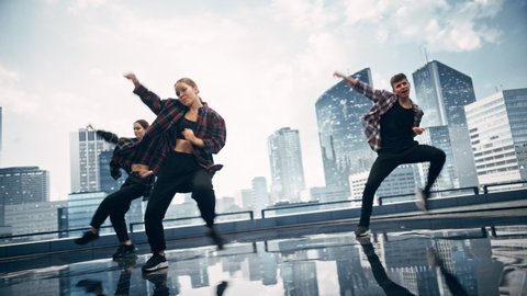 Diverse Group of Three Professional Dancers Performing a Hip Hop Dance Routine in Front of a Big Digital Led Wall Screen with Modern Urban Skyline with Skyscrapers in Studio Environment.