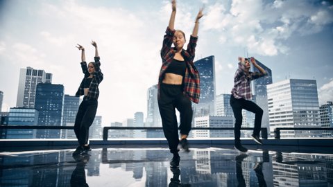Diverse Group of Three Professional Dancers Performing a Hip Hop Dance Routine in Front of a Big Digital Led Wall Screen with Modern City Skyline with Office Skyscrapers in Studio Environment.