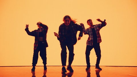 Diverse Group of Three Professional Dancers Performing a Hip Hop Dance Routine in Front of a Big Digital Led Wall Screen with Deep Warm Yellow or Orange Color Background in Studio Environment.
