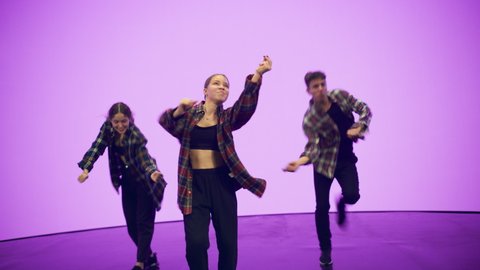 Diverse Group of Three Young Professional Dancers Performing a Hip Hop Dance Routine in Close Up in Front of a Big Led Screen with Deep Pink Color Background in Studio Environment.