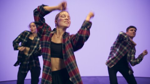 Diverse Group of Three Young Professional Dancers Performing a Hip Hop Dance Routine in Close Up in Front of a Big Led Screen with Deep Purple and Violet Color Background in Studio Environment.