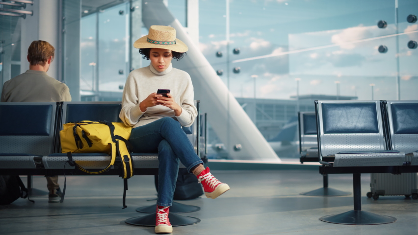Airport Terminal: Black Woman Waits for Flight, Uses Smartphone, Receives Shockingly Bad News, Misses Flight. Upset, Sad, and Dissappointed Person Sitting in a Boarding Lounge of Airline Hub. Royalty-Free Stock Footage #1084670425