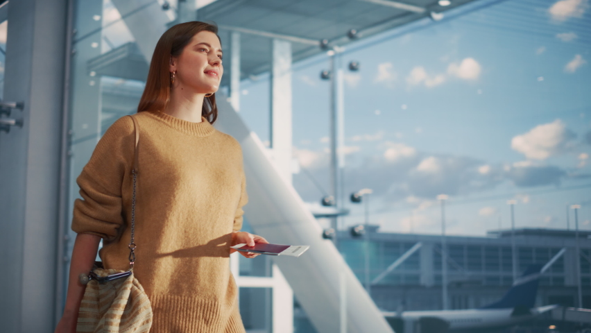 Airport Terminal: Beautiful Smiling Woman Holds Ticket, Walks Through Big Airline Hub to the Gates Where Her Airplane Waits Her. Happy Caucasian Female is Ready for Her Flight to Vacation Destination Royalty-Free Stock Footage #1084670434