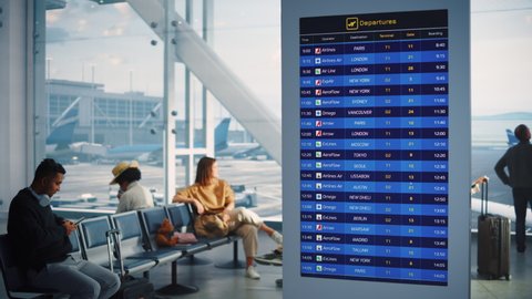 Airport Terminal: Arrival, Departure Information Display Showing all the Useful Flight Data For Travelers. Backgrond: Diverse Crowd of People Wait for their Flights in Boarding Lounge of Airline Hub