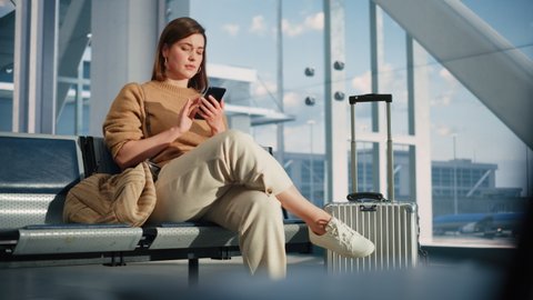 Airport Terminal: Woman Waits for Flight, Uses Smartphone, Receives Bad News, Starts Crying. Upset, Sad, and Dissappointed Person Misses Her Flight while Sitting in a Boarding Lounge of Airline Hub.