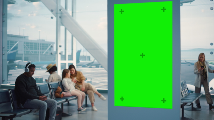 Airport Terminal: Green Screen Advertising Billboard, Arrival Display with Chroma Key, Mock-up AD Space. Backgrond: Diverse Crowd of People Wait for their Flights in Boarding Lounge of Airline Hub