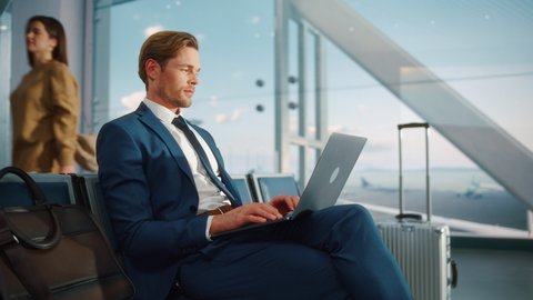 Airport Terminal: Businessman Uses Laptop Computer, Waiting for a Flight to International Conference. Traveling Entrepreneur Remote Work Online in a Boarding Lounge of Airline Hub with Airplanes