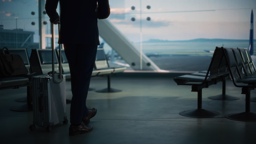 Airport Terminal: Businessman with Rolling Suitcase Walks, Uses Smartphone App for e-Business. Back View Silhouette of Traveling Man Waits for Flight in Boarding Lounge of Airline Hub with Airplanes Royalty-Free Stock Footage #1084670554