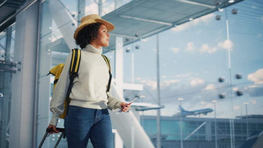Airport Terminal: Beautiful Smiling Black Woman Holds Ticket, Walks Through in Airline Hub to the Gates Where Airplane Waits. Happy African American Female is Ready for Flight to Vacation Destination Royalty-Free Stock Footage #1084670884