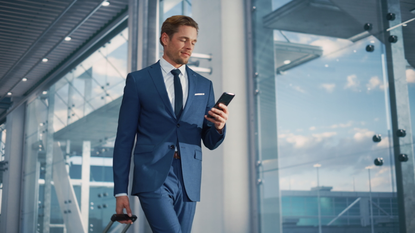 Airport Terminal: Businessman Walks to His Flight Gates, Uses Smartphone, Doing e-Business, Browsing the Internet with App. Digital Entrepreneur Remote Work Online While Traveling Through Airline Hub