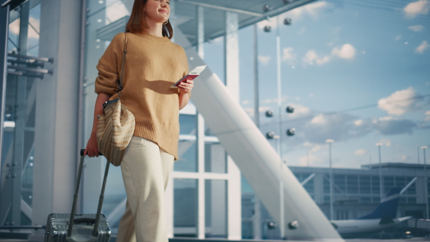 Airport Terminal: Beautiful Smiling Woman Holds Ticket, Walks Through Big Airline Hub to the Gates Where Her Airplane Waits Her. Happy Caucasian Female is Ready for Her Flight to Vacation Destination Royalty-Free Stock Footage #1084670941