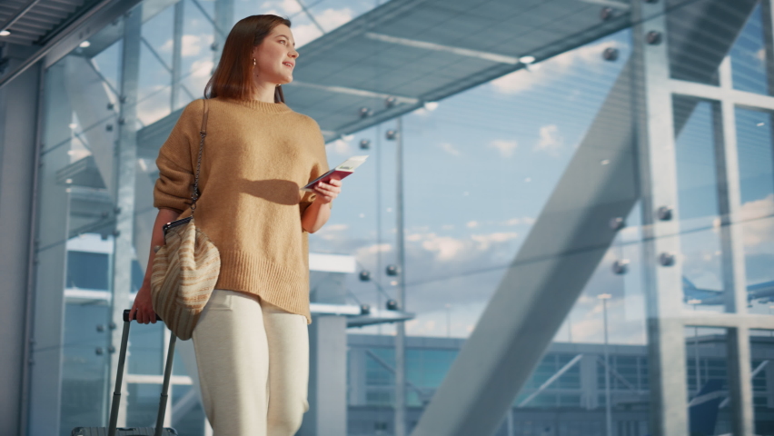 Airport Terminal: Beautiful Smiling Woman Holds Ticket, Walks Through Big Airline Hub to the Gates Where Her Airplane Waits Her. Happy Caucasian Female is Ready for Her Flight to Vacation Destination