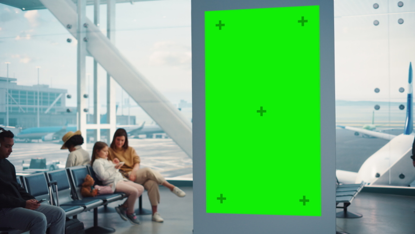 Airport Terminal: Young Man Looking for His Fligt at Green Chroma Key Screen Arrival Departure Information Display. Backgrond: Diverse People Wait for their Flights in Boarding Lounge of Airline Hub Royalty-Free Stock Footage #1084670965