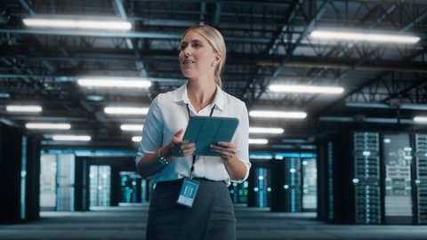 Confident Female IT Specialist Using Tablet Computer, Walk Through Big Warehouse Data Center. System Administrator working with Computing SAAS, Cloud Web Services. e-Business Digital Entrepreneur