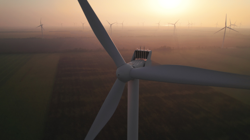 Close-up of wind turbine blades at sunset or sunrise. Windmills with rotating wings among green fields. Technology for wind energy, renewable energy source, earth care. Wind power station, drone video