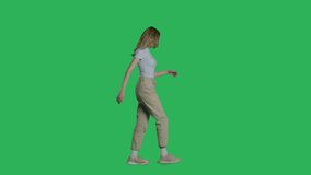 Woman in white t-shirt, jeans and sneakers walking on a Green Screen, Chroma Key. 4k UHD side view isolated video.