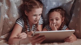 two kids girls under the blanket with a digital tablet. kid dream online video games at concept. daughters kids watching online video under covers with digital tablet. social night network media