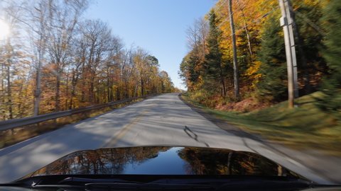 Driving black car on Vermont asphalt road full of colorful trees in Autumn season. POV