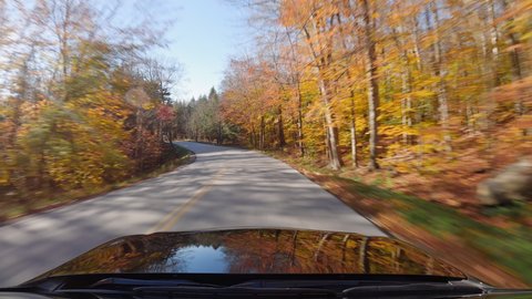 Driving a car on Vermont wood road in Autumn season. Colorful trees by the road. POV with sunlight