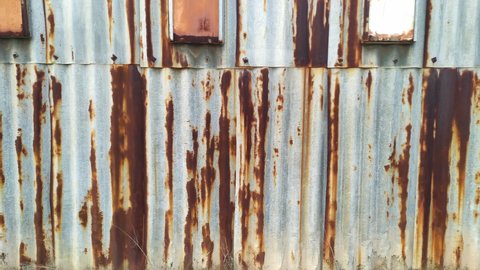 Rust on corrugated steel panels - oxidized galvanized metal sheets on the exterior wall of an old derelict building, industrial hall or warehouse. Rusty pattern of aged iron roofing on a house.