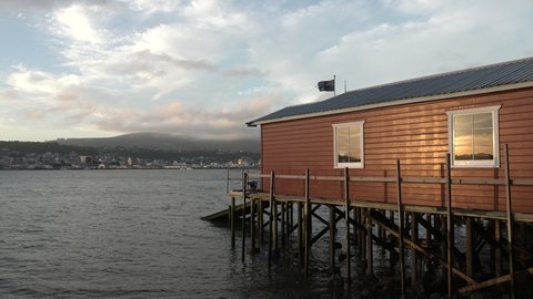 Boathouse at Otago peninsula under the soft light of the golden hour, feclectind the sunset in the windows