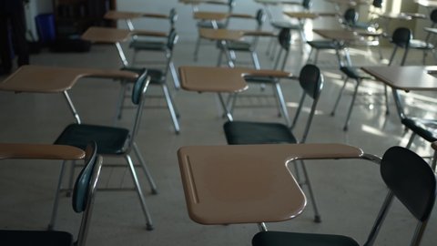 Desks in empty dark high, middle, or elementary school classroom with light coming through windows.