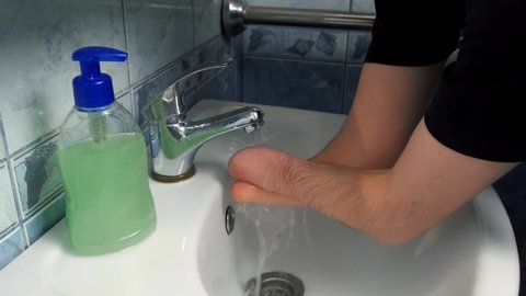 Disabled man with amputated two stump hands is washing his hands with soap at home in bathroom in sink, closeup view. Everyday routine life of a handicapped guy person with disabilities.