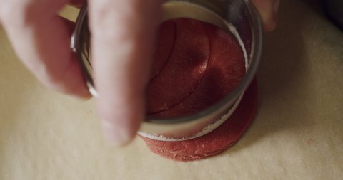 A person hand pressing down on a red cookie dough making designs, close up static