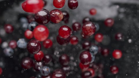 Ripe blue, black, red grapes jump up and fall on a black background with water