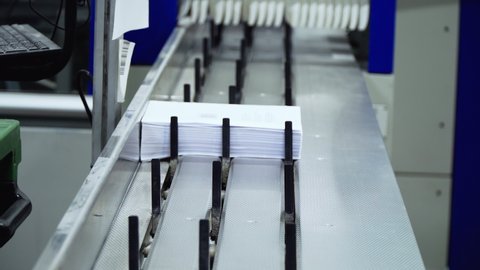 book production factory. printing of books at a specialized factory. the white man's hands gather the perfect stack of stitching sheets into a book. Conveyor production