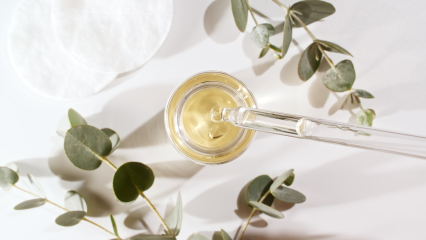 Oil drips from pipette into bottle. Eucalyptus extract, aromatic, essential oil. Cosmetics oils based on natural ingredients. Natural cosmetics production for hair and skin care. Top view. | Shutterstock HD Video #1084711558