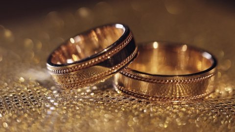 Wedding rings lying on shiny golden shining surface with light, close-up macro footage. Rotate spinning clockwise. Pair of marriage symbols. Love of bride and groom, wife and husband. Matrimony symbol