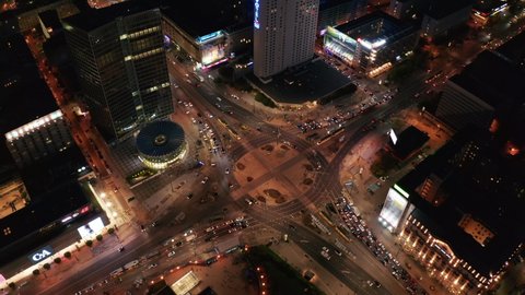 High angle view of large and busy road intersection in city at night. Two tram units passing by each other in middle of roundabout. Warsaw, Poland