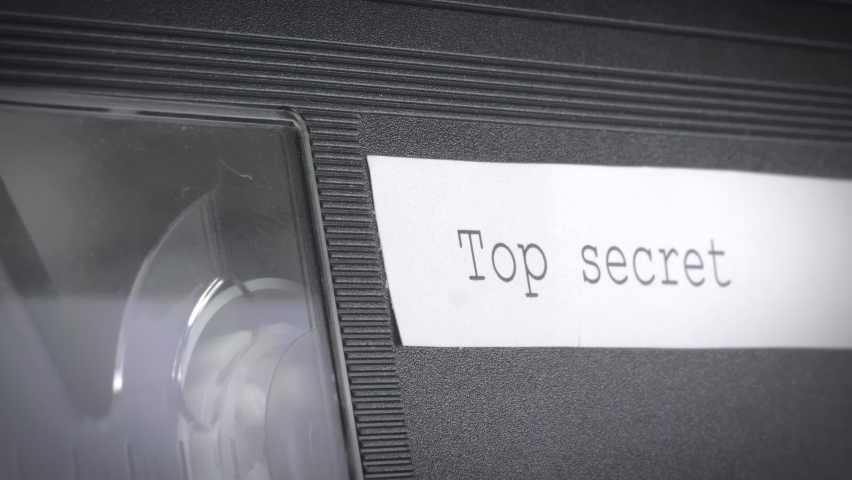 Closeup shot of an old vhs cassette mechanism with a sign that says top secret. The cassette is being inserted into a vcr. - Powered by Shutterstock - Get 15% off with code: PIKWIZARD15